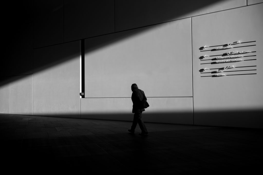 Black and white photo of a man walking alone in silhouette.