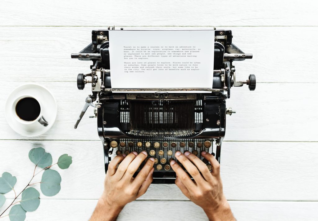 Hands poised over an old typewriter with typed page coming out.