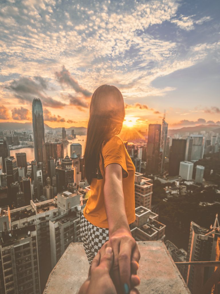 Person standing on ledge looking a city with a sunset