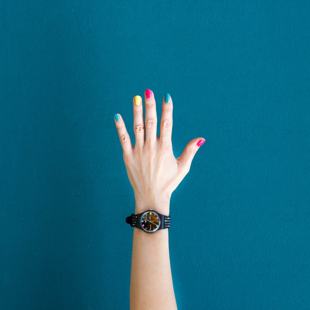Raised hand with rainboaw painted fingernails and a black watch