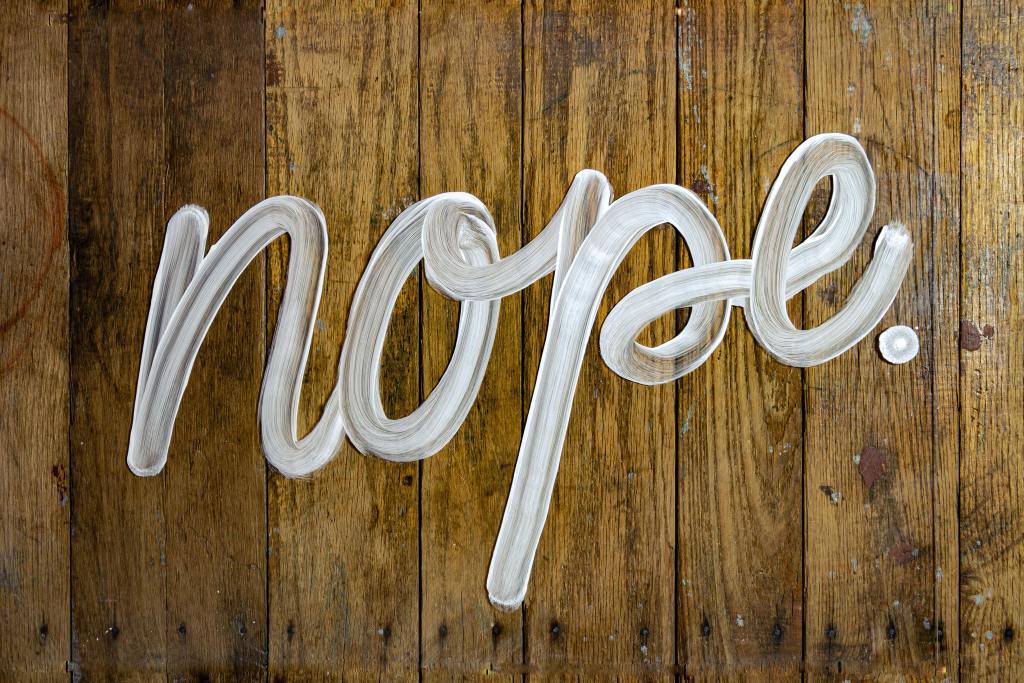 The word "nope" in clear, tubular lower case script against a wood panel background.