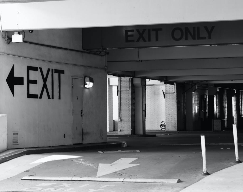 Black and white image of a wall with two windows. Wall says exit in capital letters.