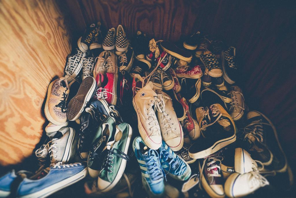 Wood panelled closet with a big pile of multiple pairs of sneakers on top of one another.