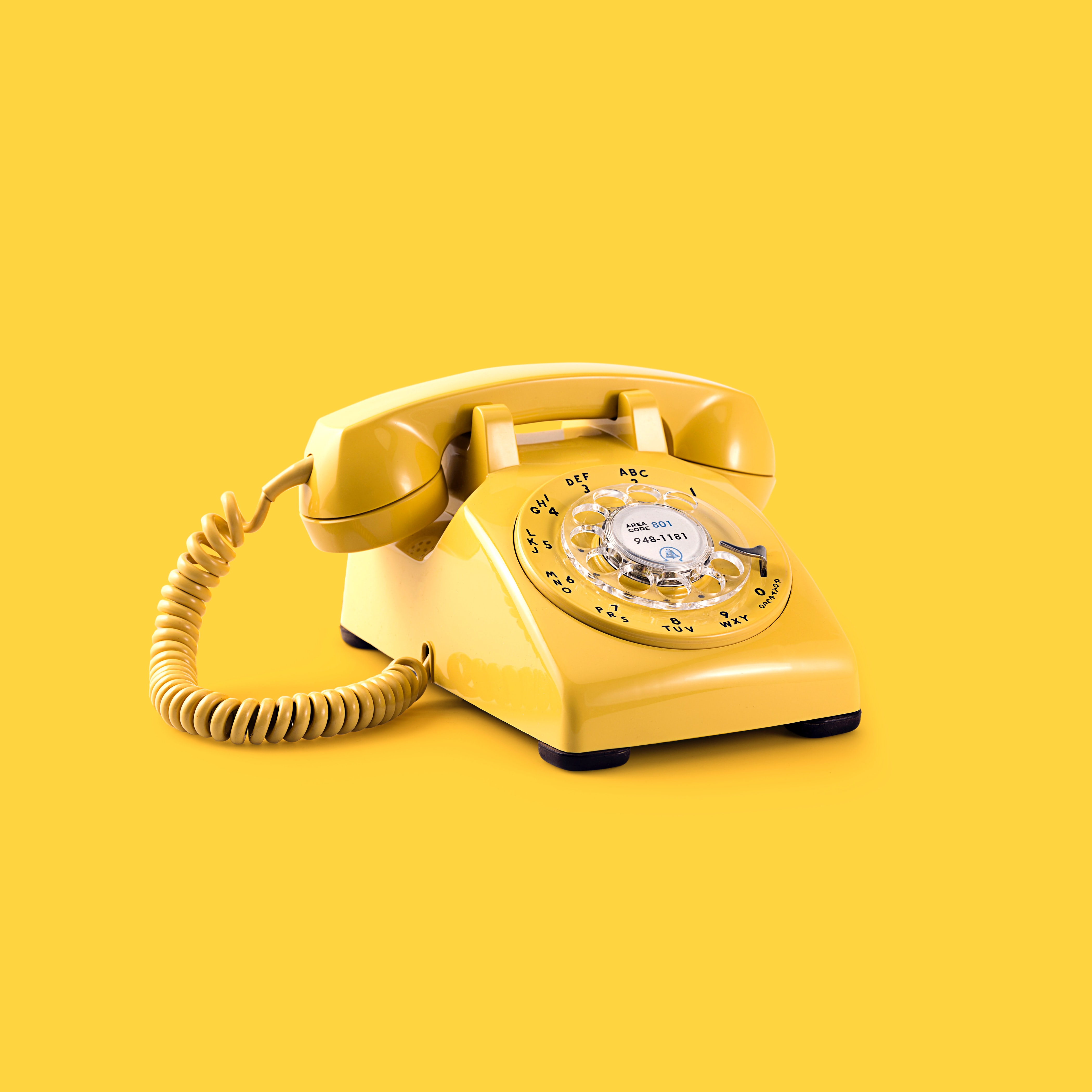 Bright yellow rotary dial telephone against a bright yellow background.