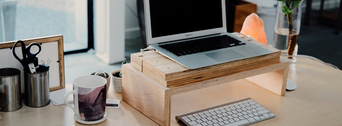 Coaching services: silver laptop on a wooden stand on a desk with a phone and mug.